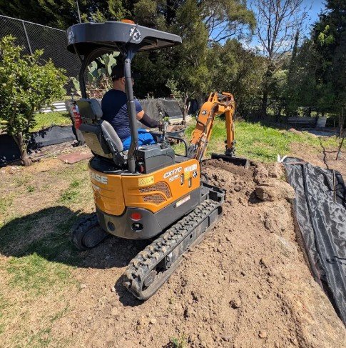 Mini excavator bucket digging a hole next to fence posts