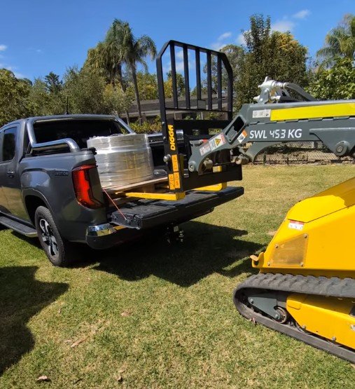 Tracked mini loader pushing a pile of bark in a garden bed